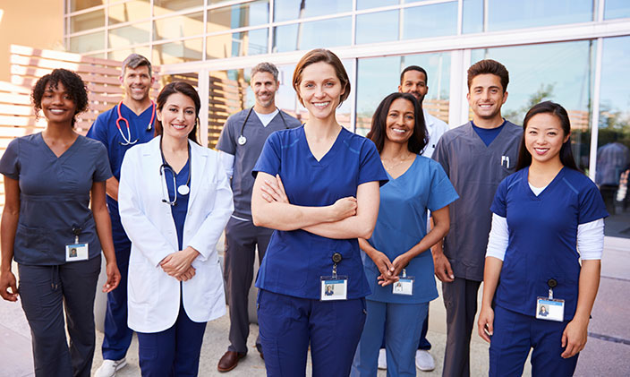 group of- healthcare professionals smiling and standing in front of hospital